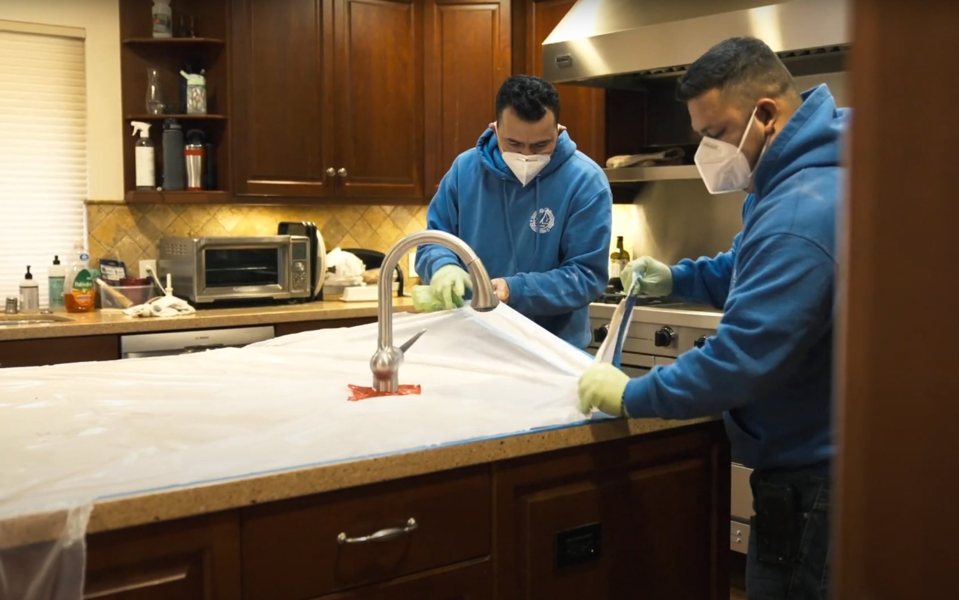 Professional water damage restoration team cleaning and sanitizing kitchen area Water damage restoration professionals working in kitchen with protective equipment